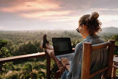woman using laptop on balcony with forest in background